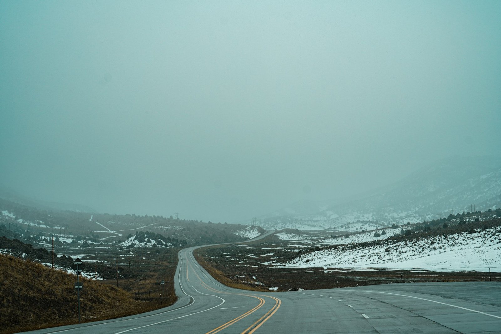 A two lane Wyoming highway curving through snow covered high plains under a grey winter sky